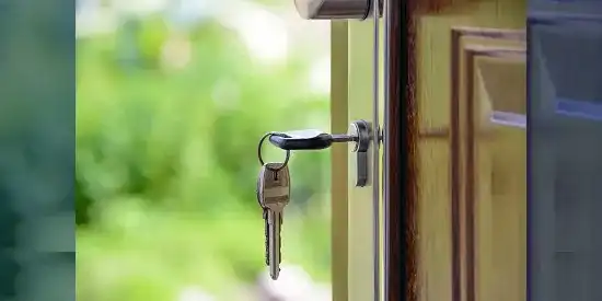 Porte ouverte avec des clés dans la serrure en premier plan et de la végétation en arrière-plan